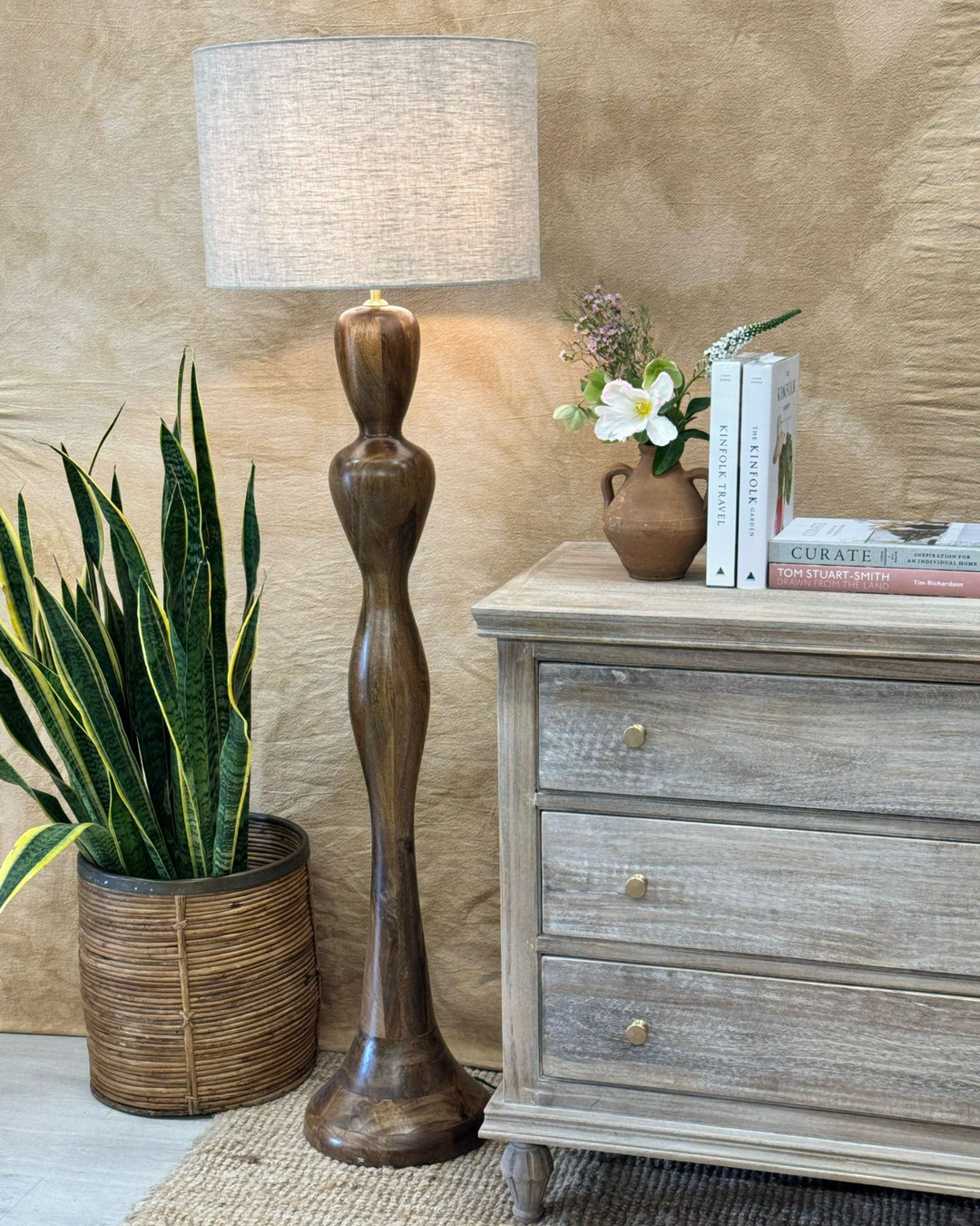 Tall, elegant floor lamp with linen base besides a whitewashed chest of draws