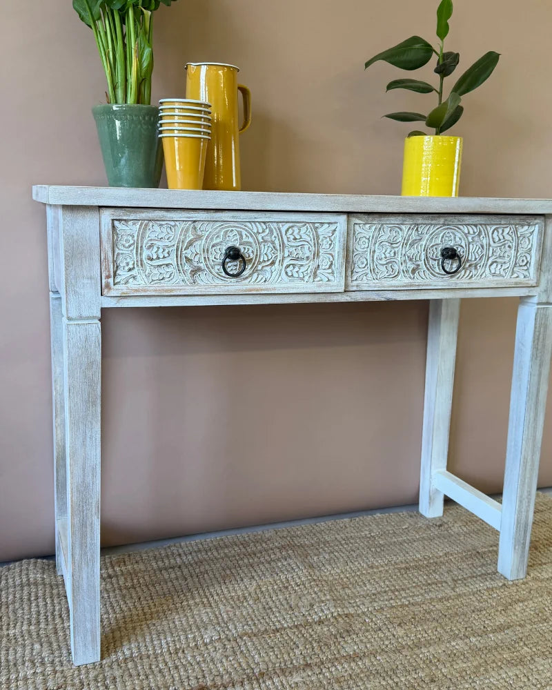 Whitewashed carved console table, angled view, styled with jugs, stacked cups and a house plant