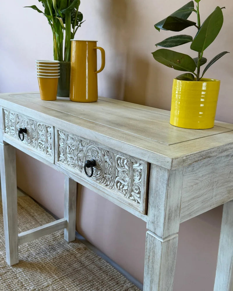 Close-up angled view of a whitewashed carved console table&