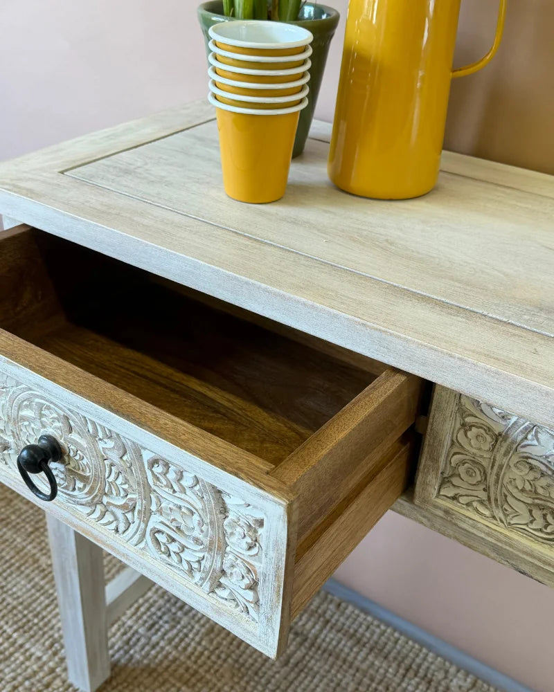 Close-up of an open drawer on a whitewashed carved console table, showing the natural wood interior against the carved front