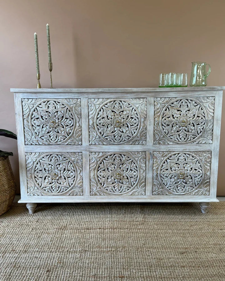 Whitewashed carved sideboard with six round floral medallion door panels, front view, styled with candlesticks and glassware