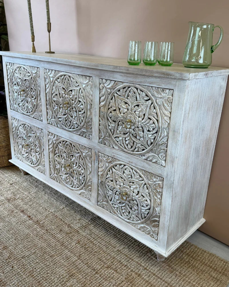Whitewashed carved sideboard with round floral medallion panels, angled side view, styled with candlesticks and glassware