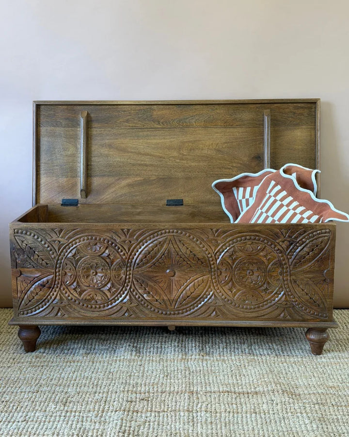 Carved mango wood blanket box, lid open, showing the carved interior lid and a rust and cream checkerboard cushion inside