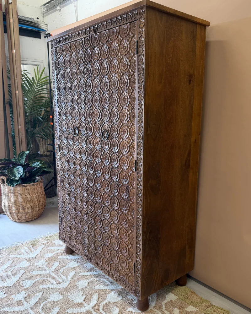 Tall carved mango wood wardrobe with floral rosette carving, angled front-side view, natural wood finish