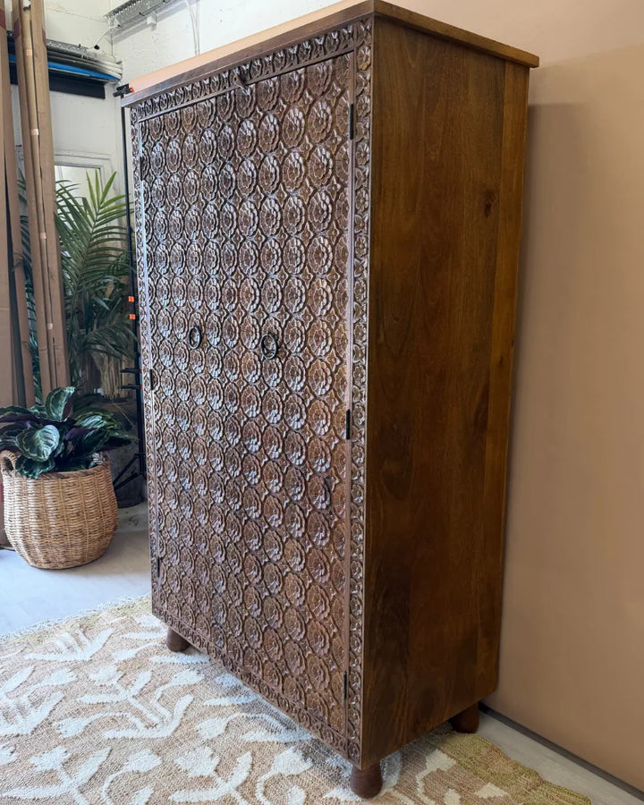 Tall carved mango wood wardrobe with floral rosette carving, angled front-side view, natural wood finish
