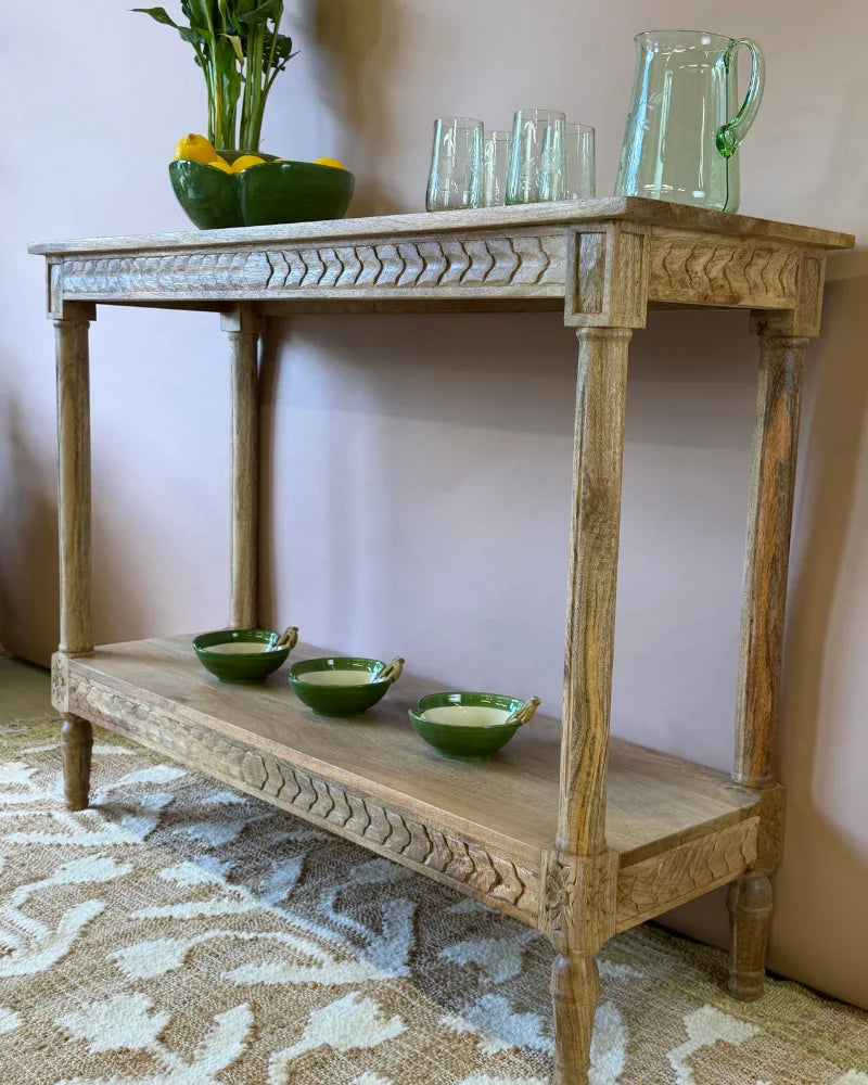 Close-up angled view of a fluted-carved console table styled with glassware and a glass jug