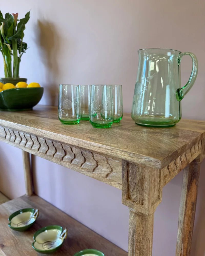 Close-up of the fluted-carved leg detail on a natural wood console table, styled with green glassware