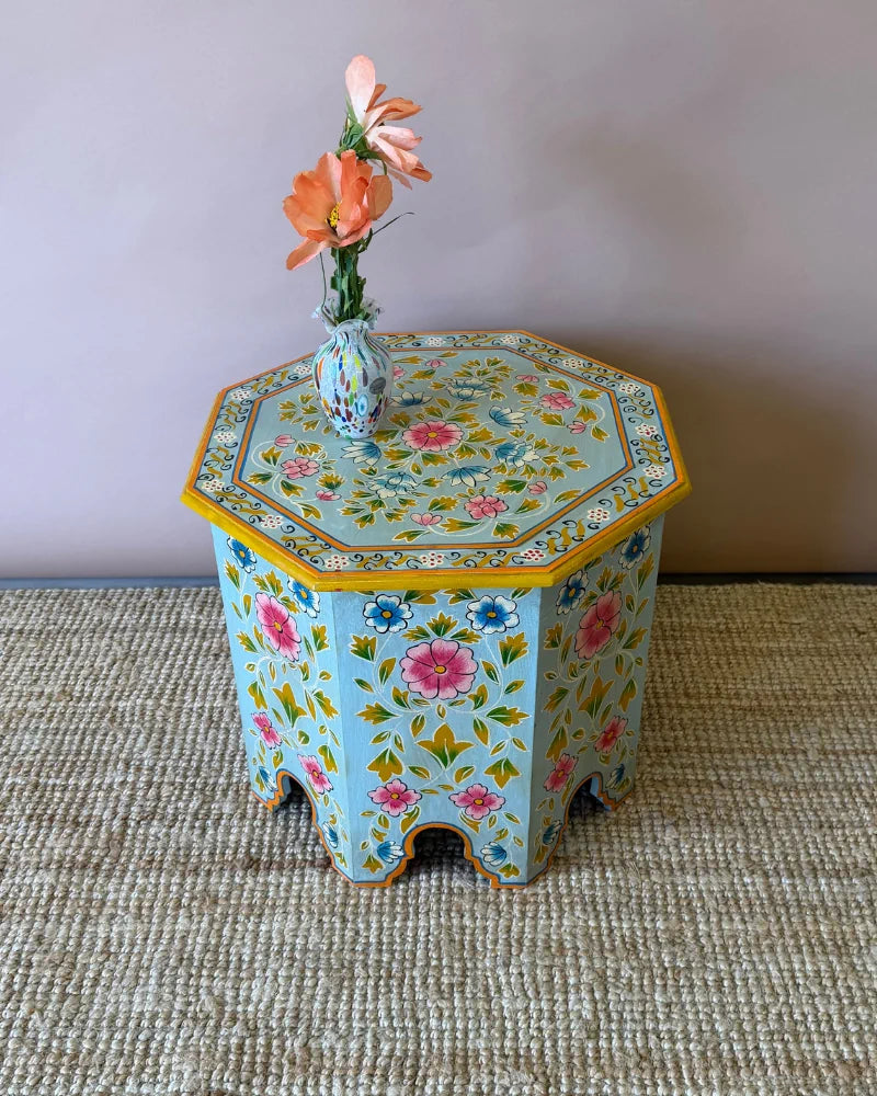 Hand-painted octagonal side table in pale blue floral design, angled view styled with a small painted vase
