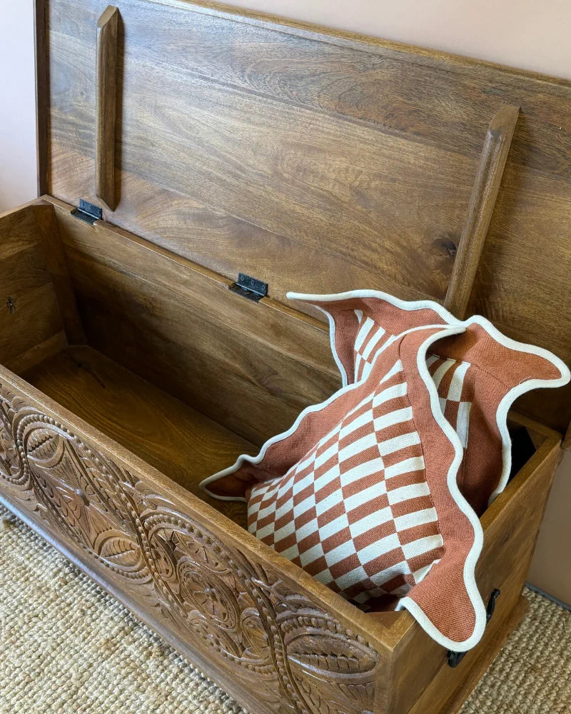 Carved mango wood blanket box, lid open, showing the carved interior lid and a rust and cream checkerboard cushion inside