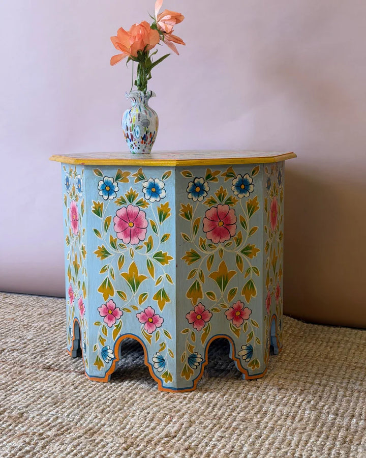 Close-up of a hand-painted octagonal side table top showing a floral medallion design in pink, blue and mustard