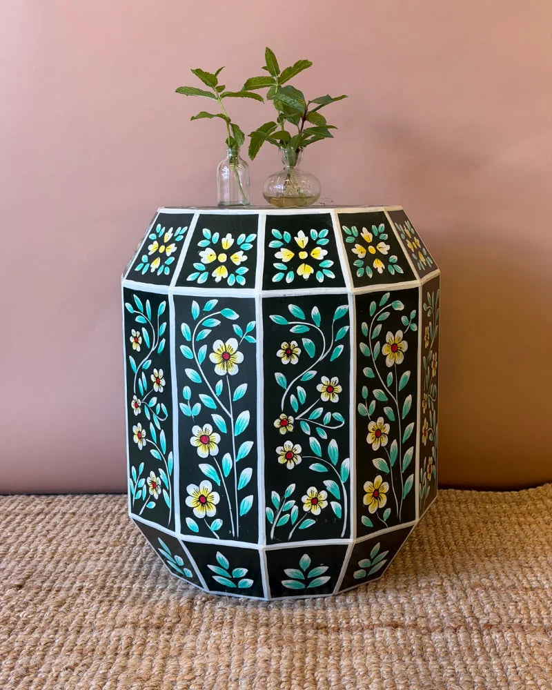 Hand-painted dark green geometric side table with white and yellow floral panel design, styled with sprigs of mint