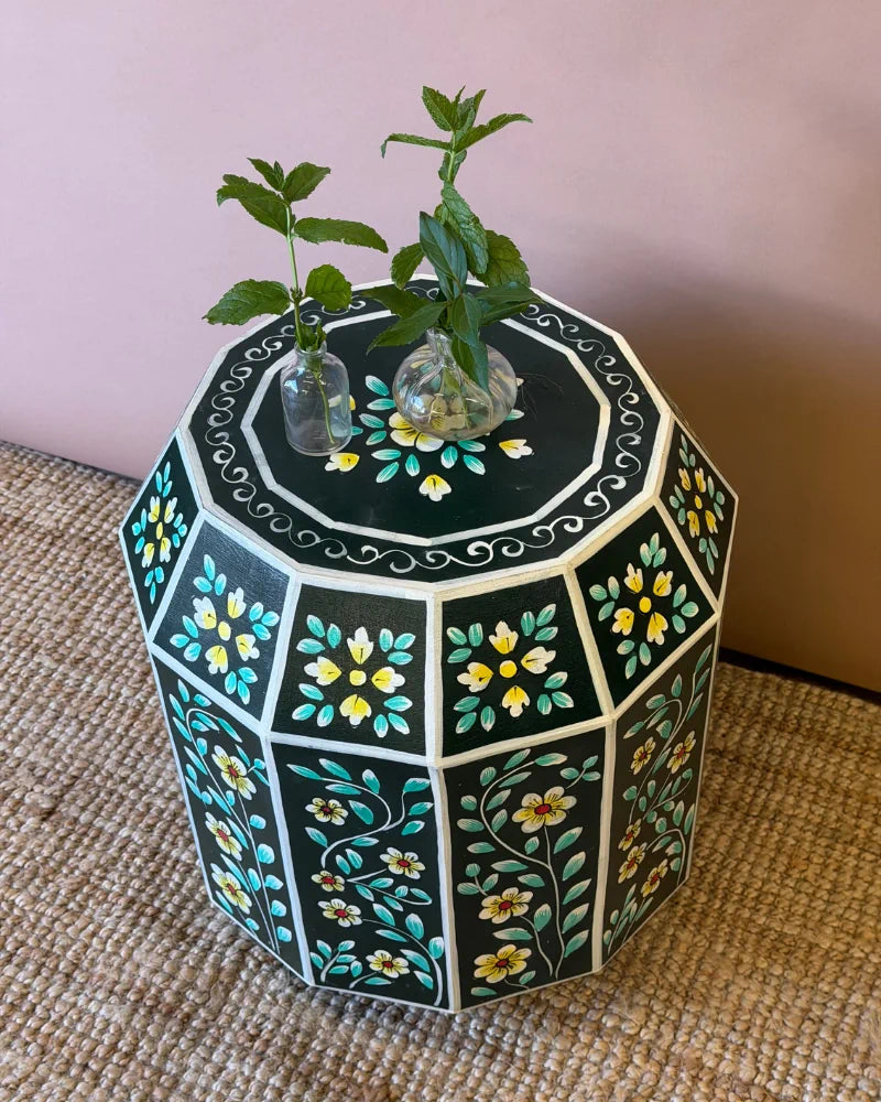 Hand-painted dark green geometric side table, angled top-down view of the floral panel design, styled with mint sprigs