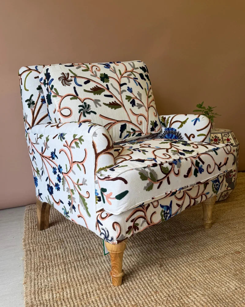 Cream armchair upholstered in botanical crewel embroidery fabric, angled side view on turned wooden legs