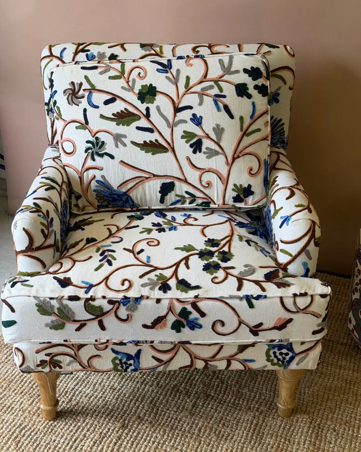 Close-up front view of a cream armchair upholstered in botanical crewel embroidery fabric