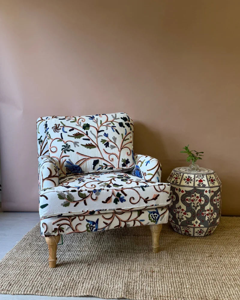 Cream crewel-embroidered armchair paired with a hand-painted drum side table, front view