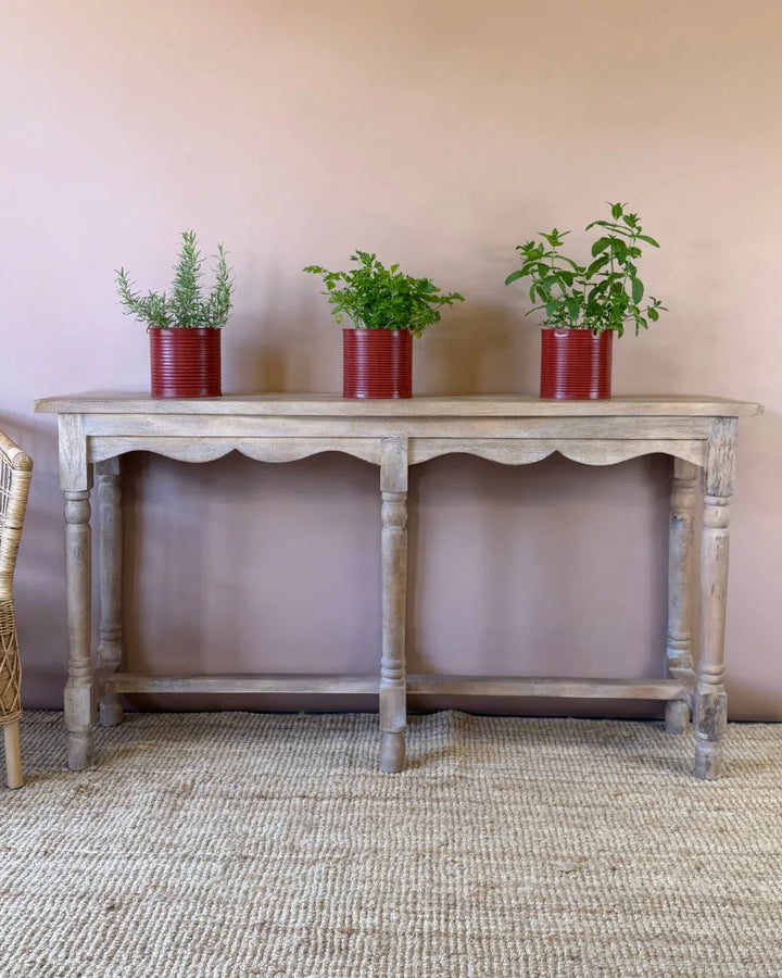 Weathered grey-wash console table with scalloped apron and turned legs, styled with herb plants in red tin planters