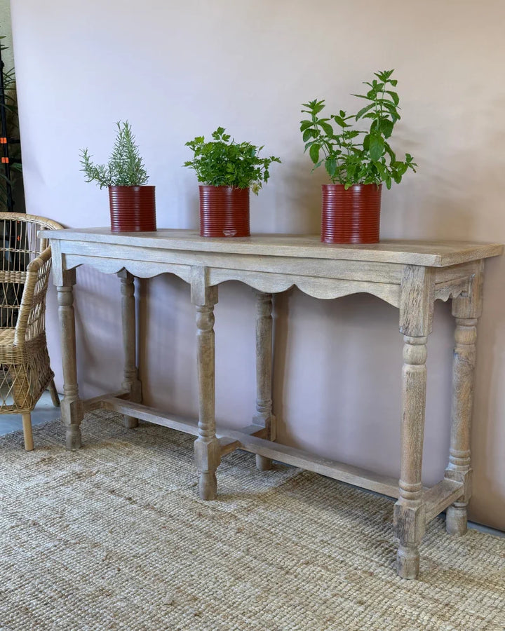 Weathered grey-wash console table with scalloped apron, angled view, styled with herb plants in red tin planters