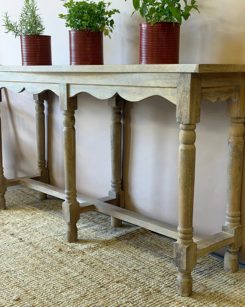 Close-up of a console table's turned leg and scalloped apron detail in a weathered grey-wash finish