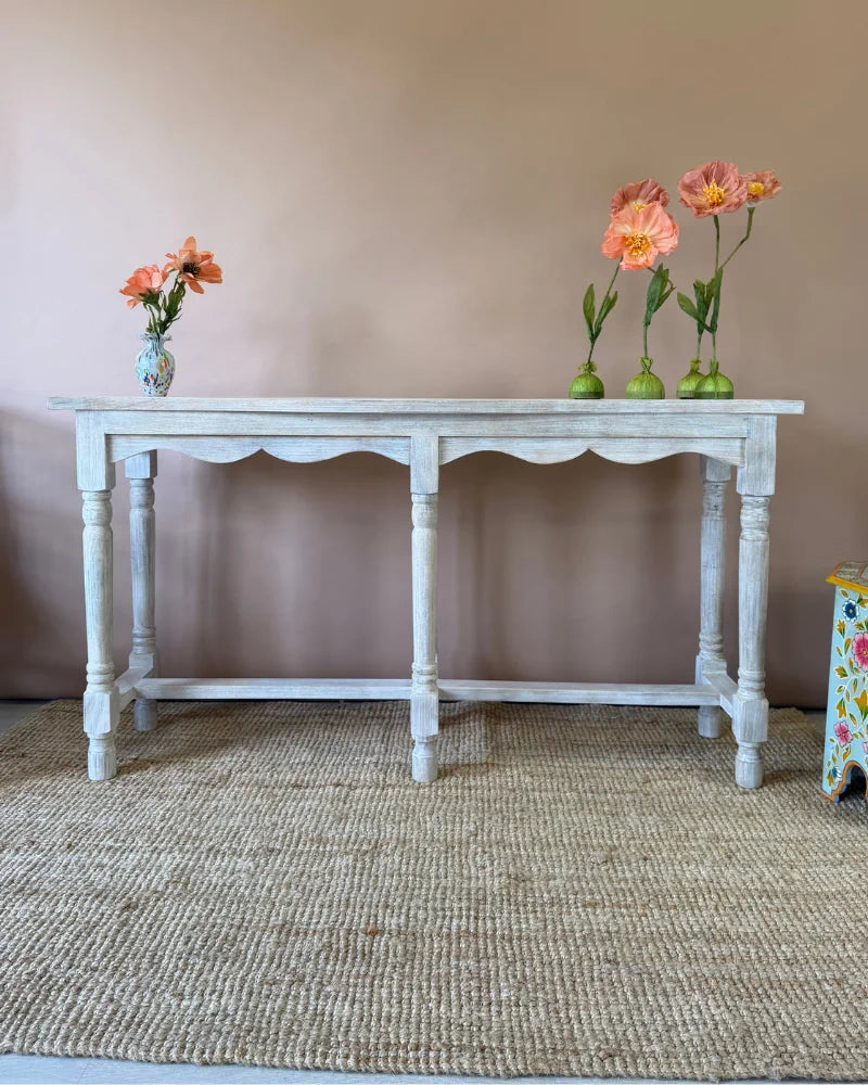 Whitewashed console table, angled view, styled with poppy flower stems and a painted ceramic vase