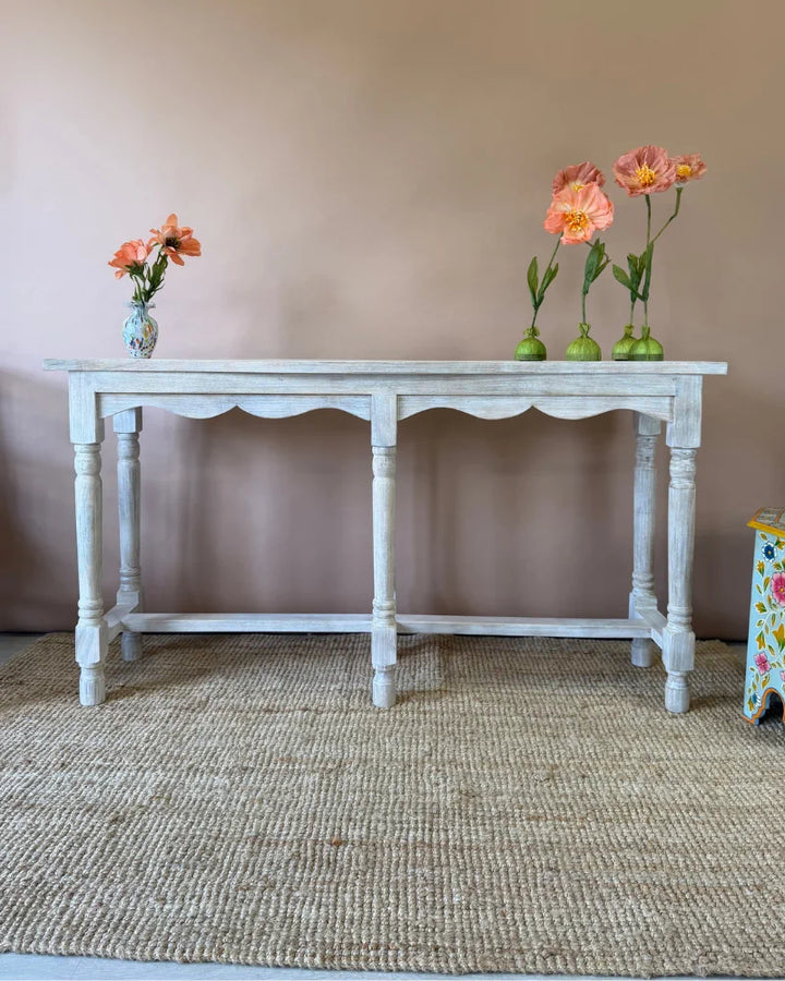 Whitewashed console table, angled view, styled with poppy flower stems and a painted ceramic vase