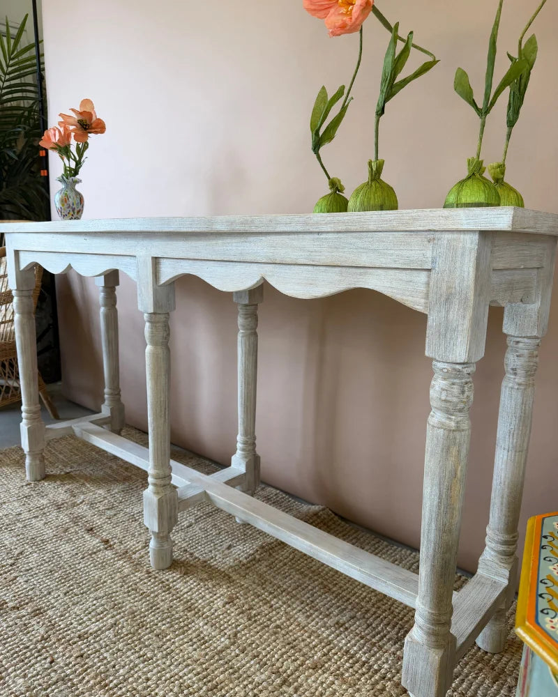 Close-up angled view of a whitewashed console table styled with poppy flower stems in small green vases
