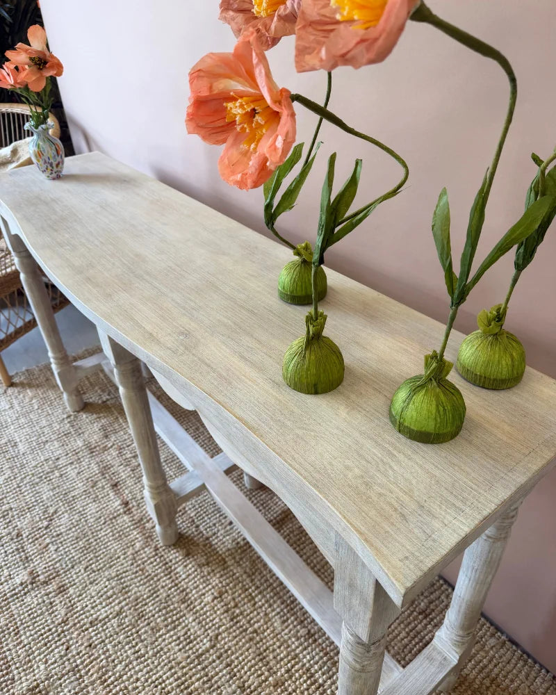 Close-up top-down view of a whitewashed console table styled with poppy flower stems in small vases