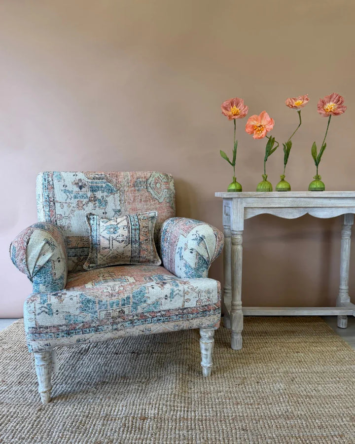 Armchair in vintage rug-print patchwork fabric with a matching lumbar cushion, beside a console table styled with poppies