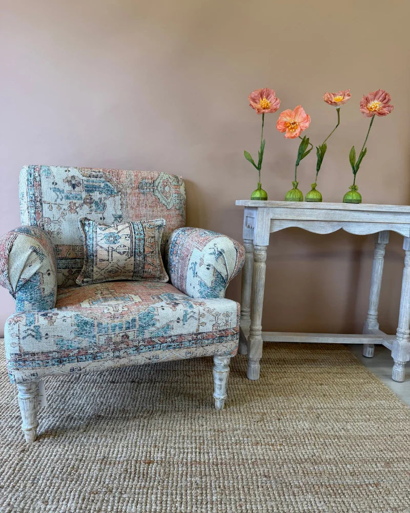 Armchair in vintage rug-print patchwork fabric with a lumbar cushion, front view beside a whitewashed console table