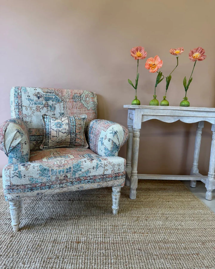 Armchair in vintage rug-print patchwork fabric with a lumbar cushion, front view beside a whitewashed console table