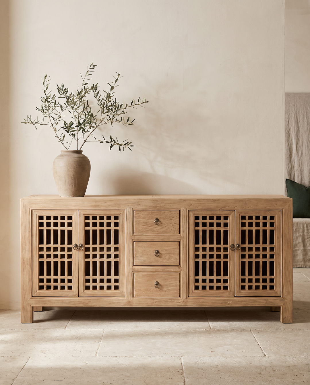 A light natural wood sideboard cabinet with lattice-patterned doors and three central drawers, styled in a minimalist room with a ceramic vase of branches on top.
