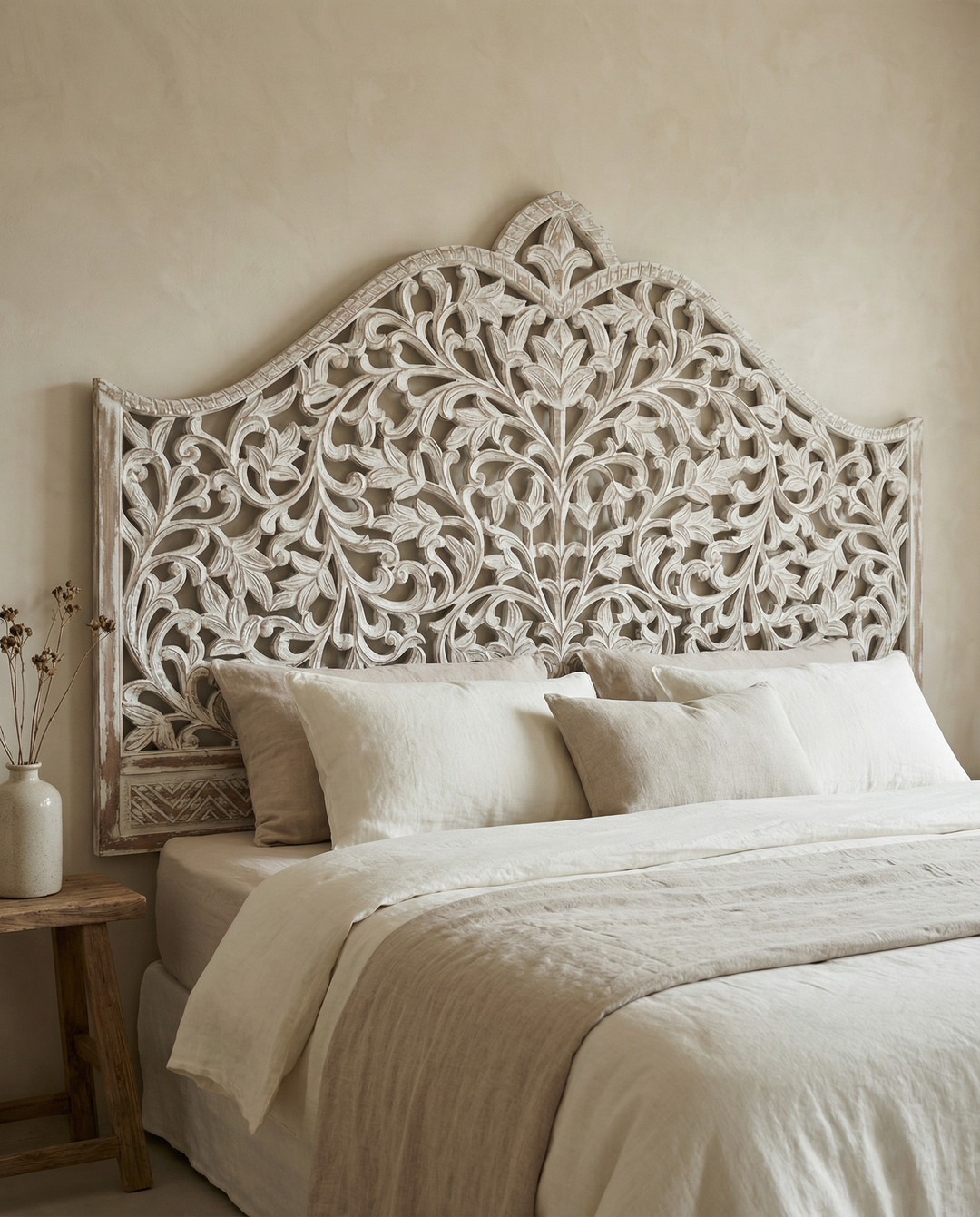 Decorative headboard with intricate carvings above a bed with white bedding.