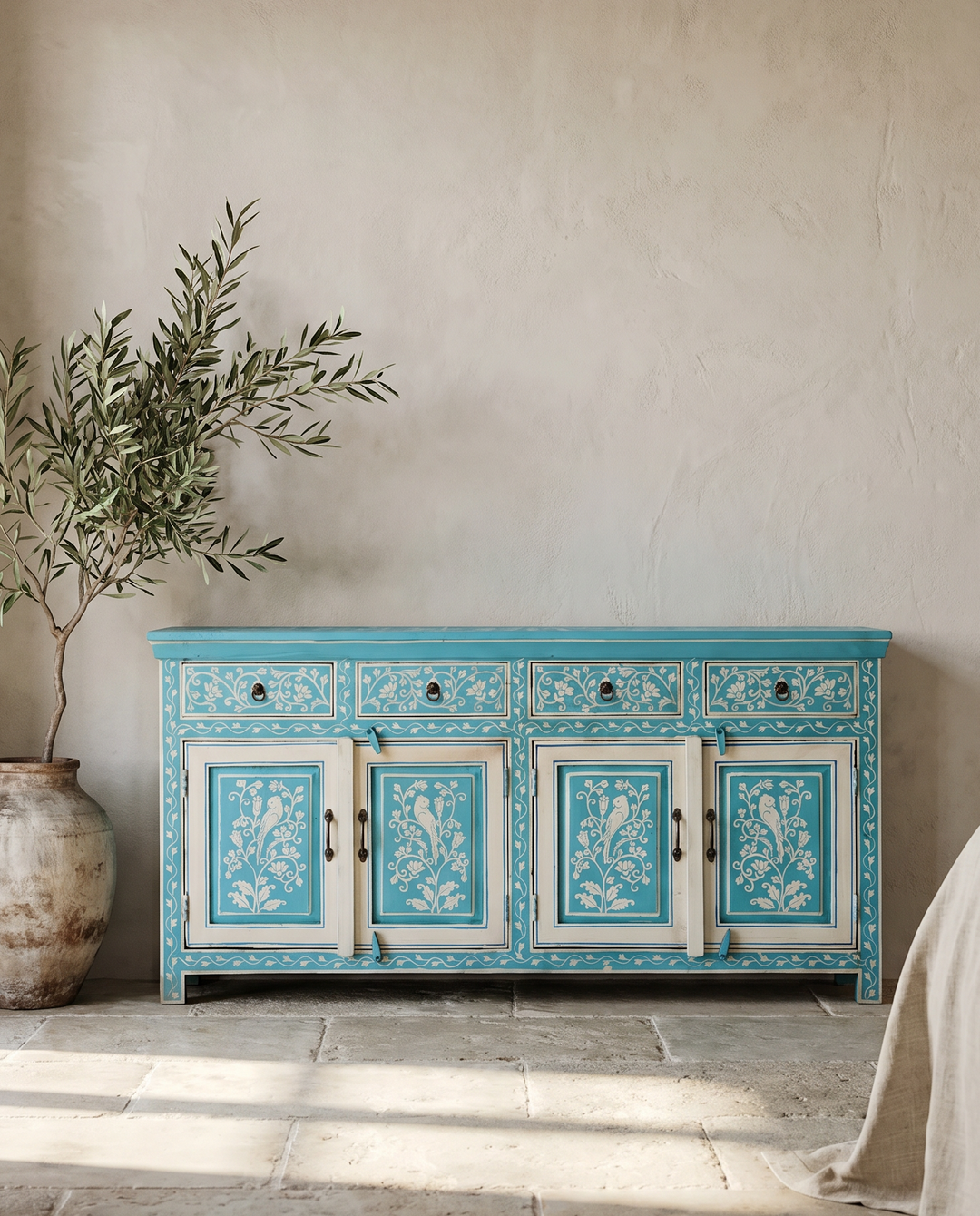 Blue ornate sideboard with floral patterns in a room with a plant and draped fabric.